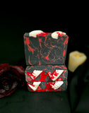Black soap bars with red swirls  with vampire fangs and blood splatter on top with a dark rose and candle on a black background.