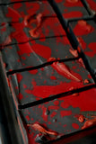A close-up of a bar of handcrafted soap with a red and gray color pattern, resembling a smoky wood or amber fragrance.