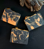 Three bars of black and orange soap with a logo on a dark surface