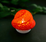 Mushroom-shaped tealight with a textured red cap and white bottom on a dark background