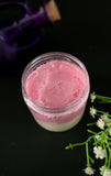 Pink and white layered sugar scrub in a jar with flowers on a dark background