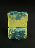 Bars of green and blue soap with soap leaves on top, stacked on a black background