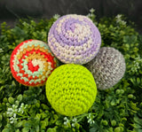 Four crocheted balls in different colors on a green leafy background