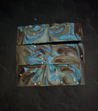 Soap bars in dark purple and silver accents on a black background shown from the top down.