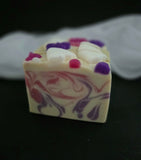 Stacked bars of handmade soap with a cream base, featuring swirls of pink and purple, embedded white ghosts and purple and pink bows on top, set against a black background with a white fabric prop.