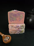 Pink soap with green and purple  swirls with herbs on top on a black background.