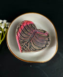 Heart shaped soap with rib cage design in black and pink colors on a white plate against a dark background
