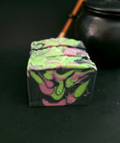 Black soap bar with bright green and purple swirls on a black background.