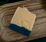 Stacked soap bars with natural turmeric color and activated charcoal on the bottom. Honey comb texture on top with calendula petals on a wood background