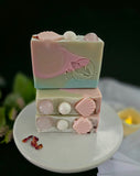 Pink and blue decorative soaps with seashell and pearl embellishments on a white plate.
