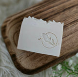 White soap bar with a feather design on a wooden surface