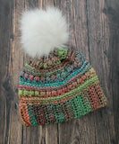 Multicolored rainbow crochet beanie with a white pom-pom on a wooden surface