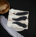 Cream and grey swirled soap with white soap raven skull and  black soap bird feather on top and a touch of eco glitter.