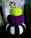 Three crocheted pumpkins in green, purple, black and white striped with a wooden worm "stem".