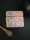 Top view of pink soap with green and purple  swirls with herbs on top on a black background.