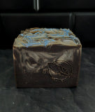 Soap bar in dark purple and silver accents on a black background.