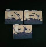 Three rectangular handmade soap bars with a Halloween theme, featuring a cream and dark purple marbled design with a crescent moon and bats, displayed on a black background.