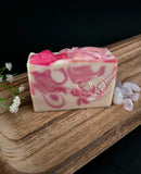 Pink and white swirled soap bar on a wooden surface with small flowers.