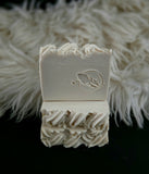 White soap bar with decorative top and leaf design on a fluffy white background