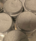 Charcoal foaming scrubs in clear containers on a reflective surface