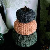 Three crocheted pumpkins in black, orange and green with a faux leather leaf.
