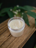 Jar of white sugar scrub on a wooden surface with green leaves in the background
