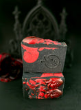 Two black soap bars with red designs stacked on a dark background