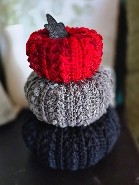 Three crocheted pumpkins in red, gray, and black with a faux leather leaf.