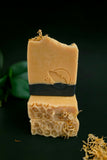 Stacked soap bars with natural turmeric color and activated charcoal on the bottom. Honey comb texture on top with calendula petals on a dark background