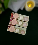 Top of three decorative soap bars with shell and flower designs including a rose quartz crystal on top on a dark background.