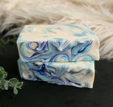 Marbled blue and white soap bars on a dark surface with a fluffy white background