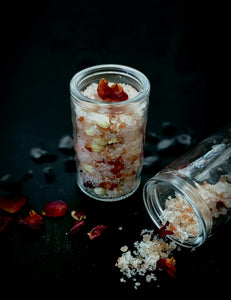 Enchanted Berry Ritual Soaking Salt with dried rose petals and jasmine buds, pictured in black bag and corked jar