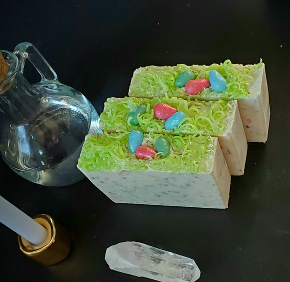 Ostara Coconut Milk Artisan Soap. White soap bar with rainbow speckles, soap grass and eggs on top.