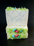 Ostara Coconut Milk Artisan Soap. White soap bar with rainbow speckles, soap grass and eggs on top.