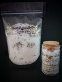 White bath salts with lavender and jasmine buds pictured in a black bag and corked jar