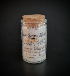 White bath salts with lavender and jasmine buds pictured in a black bag and corked jar