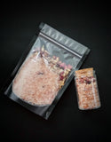 Enchanted Berry Ritual Soaking Salt with dried rose petals and jasmine buds, pictured in black bag and corked jar